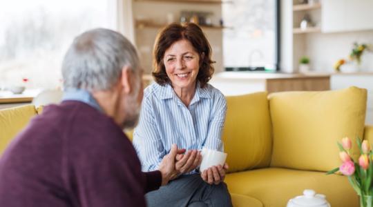 Older adults holding hands on a couch at home